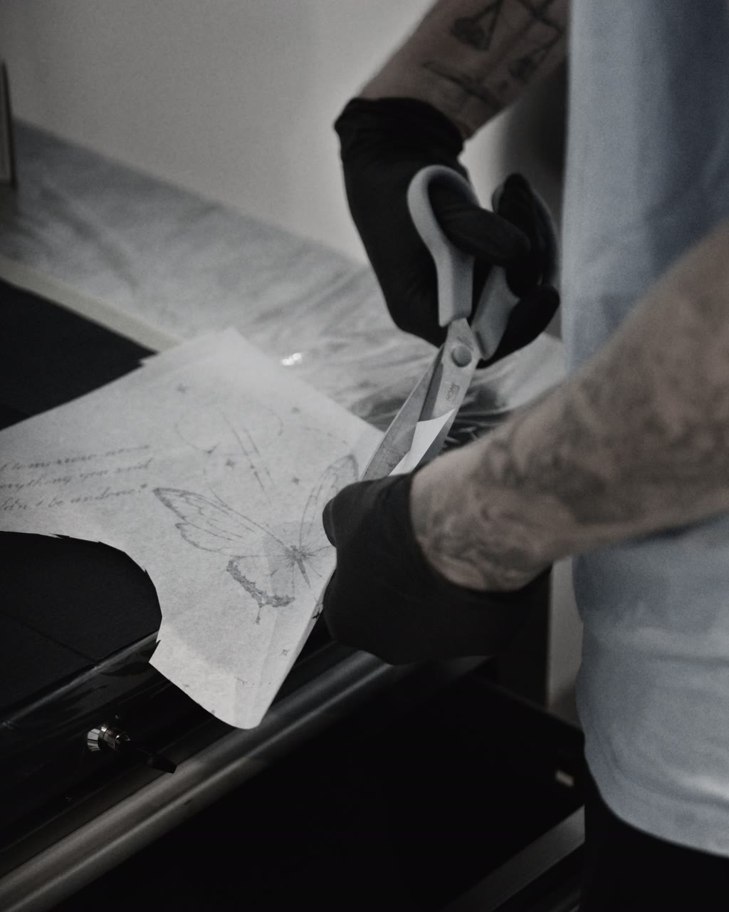 Behandschuhte Hände schneiden eine Tattoo-Schablone mit der Schere zu